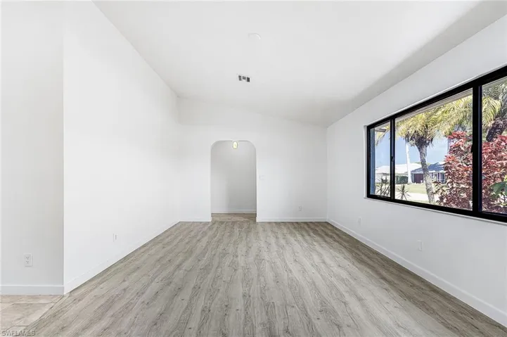 Spacious living area featuring wood-finish flooring, vaulted ceilings, and a large window with black framing