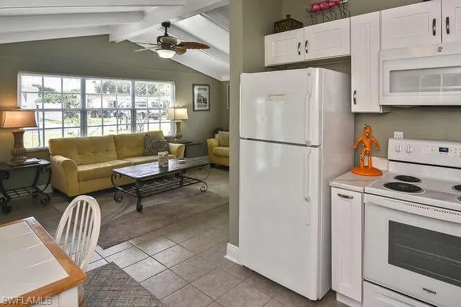 Kitchen featuring white appliances, light tile patterned floors, white cabinets, a ceiling fan, and open floor plan
