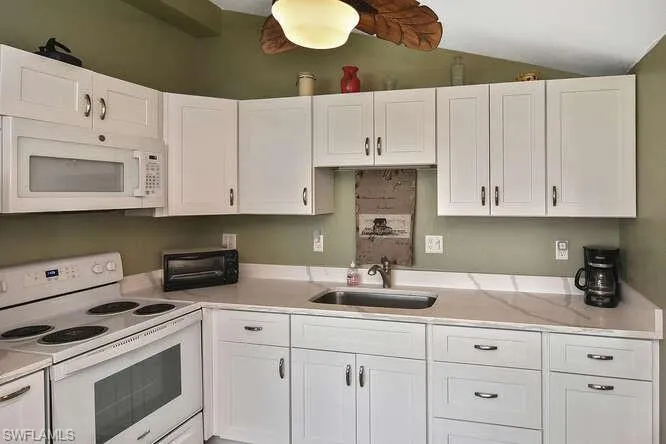 Kitchen with white appliances, light countertops, white cabinets, and vaulted ceiling