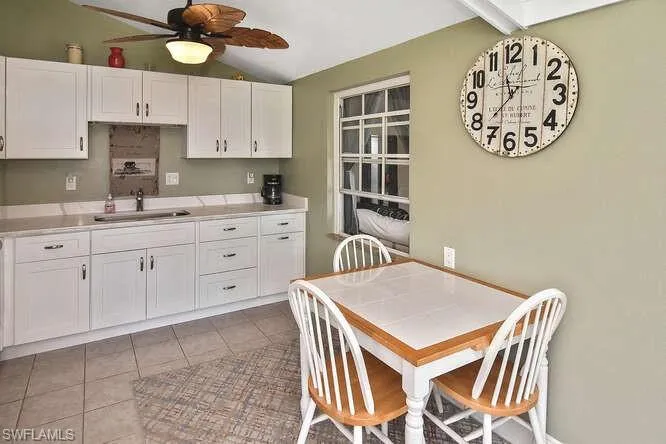 Kitchen featuring lofted ceiling, ceiling fan, white cabinetry, light tile patterned flooring, and light countertops