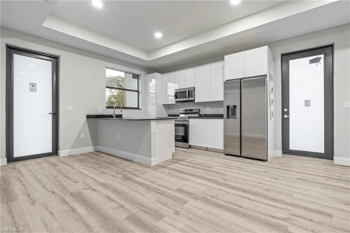 Kitchen featuring white cabinetry, a peninsula, stainless steel appliances, modern cabinets, and dark countertops