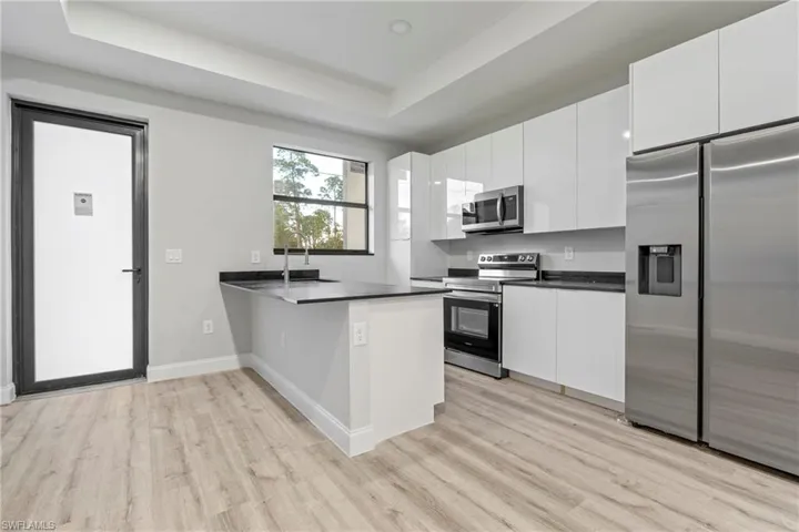 Kitchen with stainless steel appliances, a peninsula, a tray ceiling, white cabinetry, and light wood finished floors