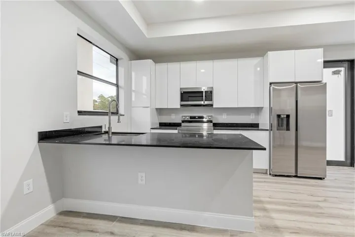 Kitchen featuring stainless steel appliances, modern cabinets, dark stone countertops, and light wood finished floors