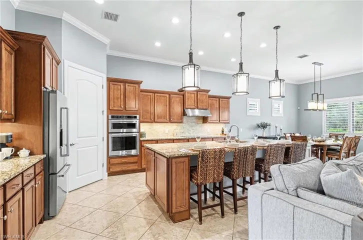 Kitchen with wood finish cabinets, a kitchen breakfast bar, a kitchen island with sink, light stone counters, and stainless steel appliances
