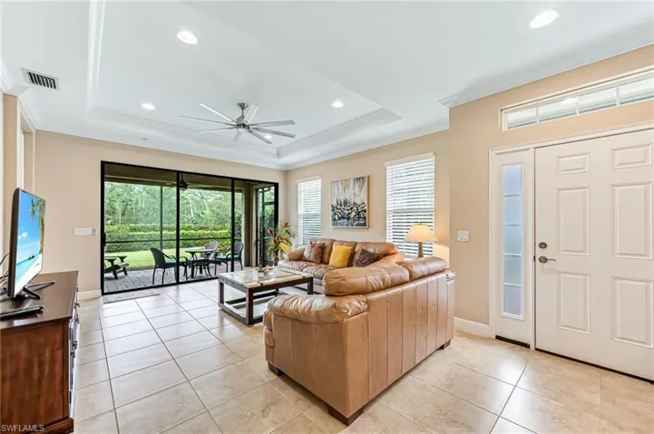 Living room with ceiling fan, ornamental molding, a tray ceiling, light tile patterned flooring, and baseboards