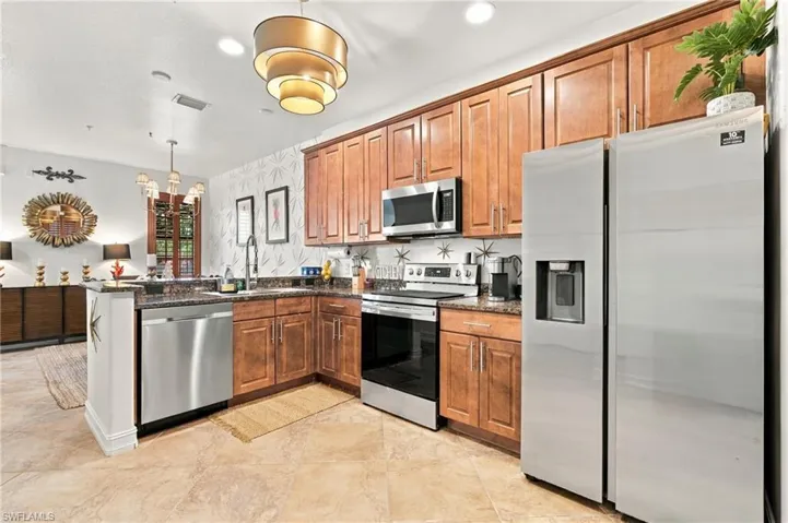 Kitchen featuring medium-tone wood cabinetry, stone-finish countertops, stainless steel appliances, tile flooring, and a multi-tiered pendant light fixture