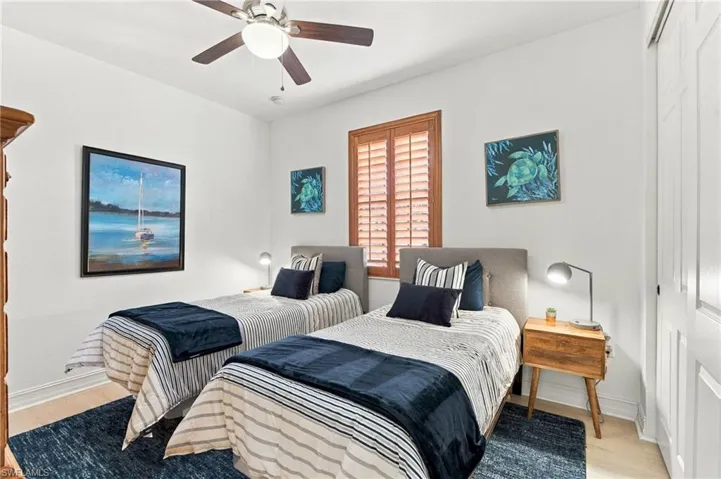 Bedroom featuring wood-finish flooring, ceiling fan with integrated lighting, window with stained wood shutters, and dual-panel closet doors
