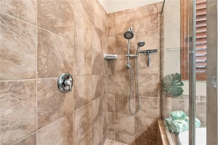 Shower enclosure featuring floor-to-ceiling stone-patterned tile, chrome dual-head shower fixtures, a built-in corner shelf, and a glass door