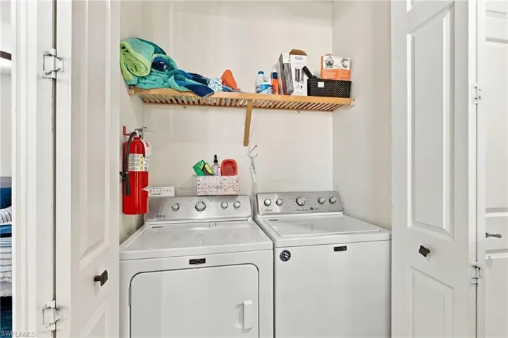 Laundry alcove featuring white, top-load appliances and a slatted wood wall-mounted shelf