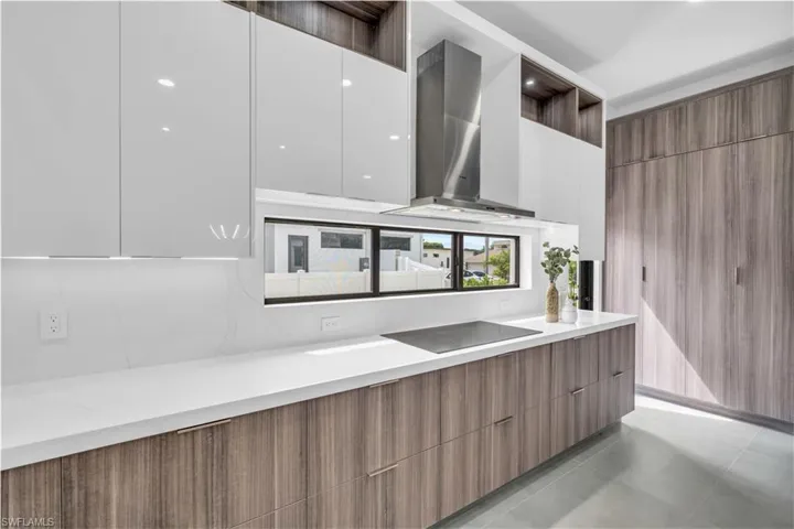 Kitchen featuring light tile patterned flooring, white cabinetry, black electric cooktop, and wall chimney exhaust hood