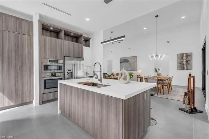 Kitchen featuring a center island with sink, stainless steel appliances, a towering ceiling, decorative light fixtures, and sink