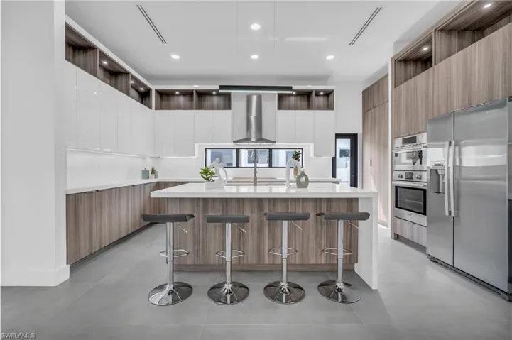 Kitchen featuring white cabinetry, a breakfast bar area, wall chimney range hood, appliances with stainless steel finishes, and a large island with sink