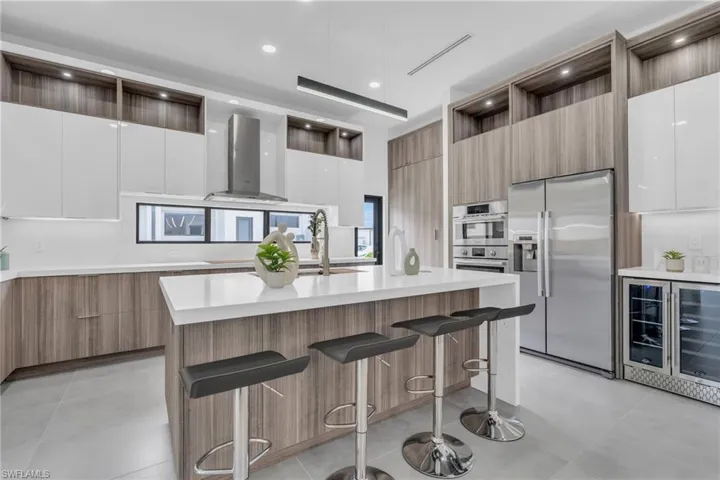 Kitchen featuring white cabinetry, stainless steel appliances, wall chimney exhaust hood, a kitchen breakfast bar, and a center island with sink