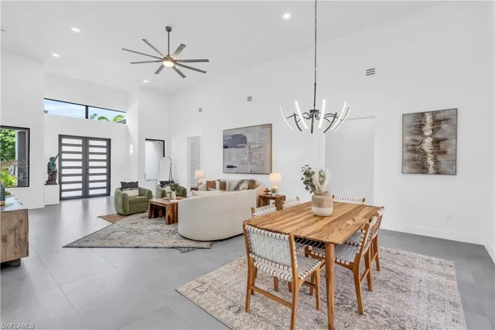 Dining space with tile patterned floors, ceiling fan with notable chandelier, and a towering ceiling