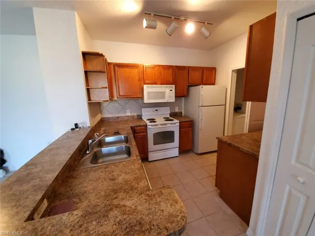 Kitchen with white appliances, a sink, open shelves, brown cabinetry, and backsplash