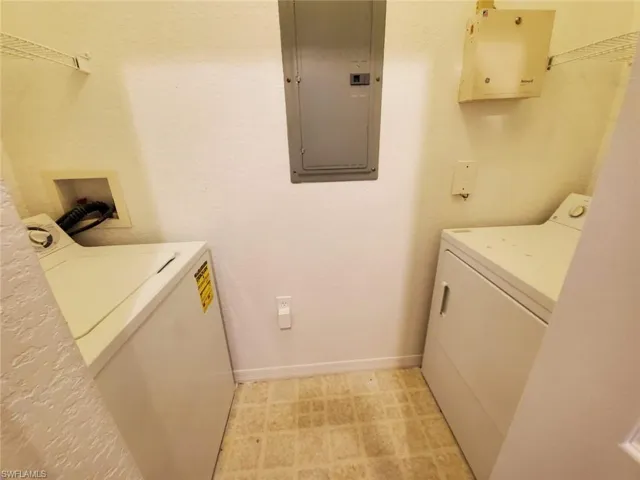 Laundry area with electric panel, washer and dryer, baseboards, and light floors
