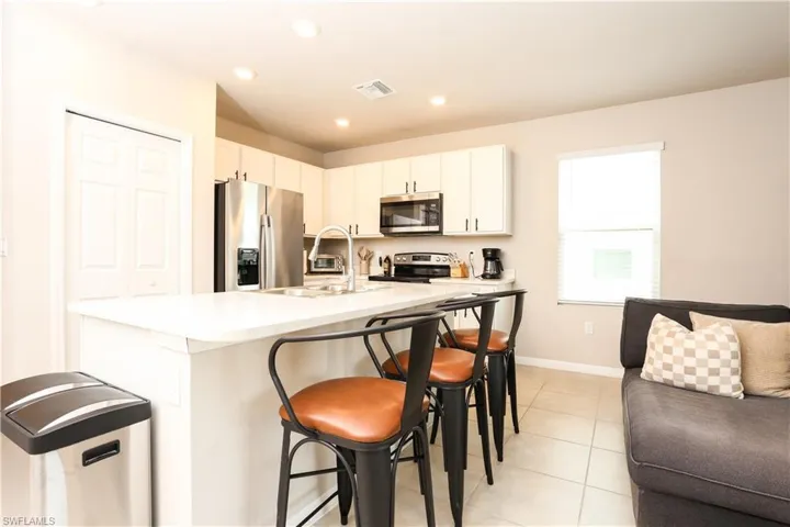 Kitchen with appliances with stainless steel finishes, a kitchen bar, light tile patterned floors, white cabinetry, and a kitchen island with sink