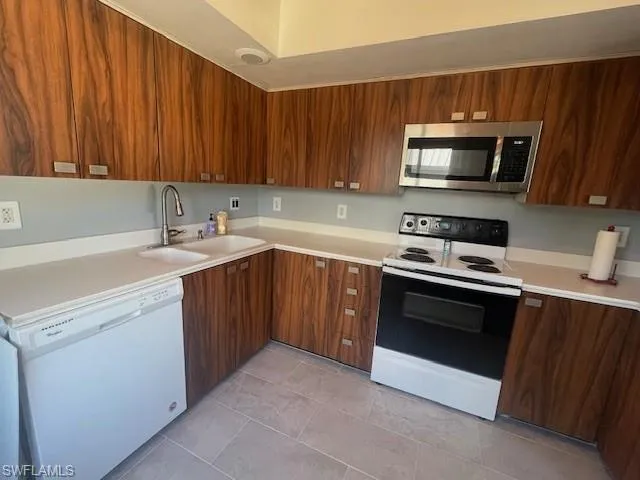 Kitchen with range with electric cooktop, white dishwasher, stainless steel microwave, and light countertops