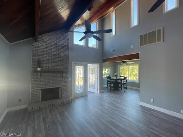 Unfurnished living room with wood ceiling, ceiling fan, dark wood-style flooring, high vaulted ceiling, a brick fireplace, and beamed ceiling