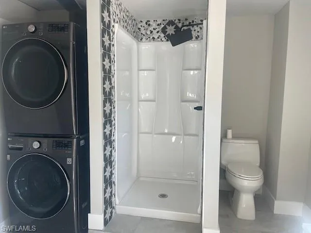 Full bath featuring estacked washer and dryer, a stall shower, and tile patterned flooring