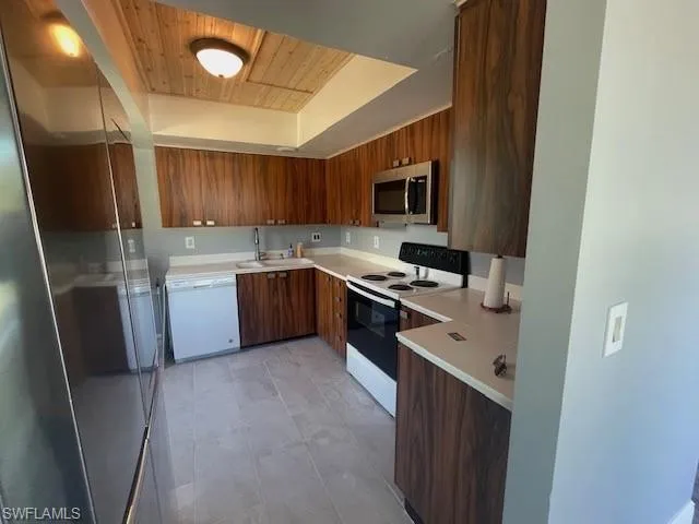 Kitchen featuring electric range, light countertops, brown cabinets, modern cabinets, and white dishwasher