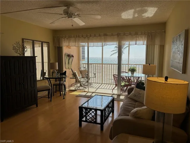 Living room with ceiling fan, light hardwood / wood-style floors, a water view, and a textured ceiling