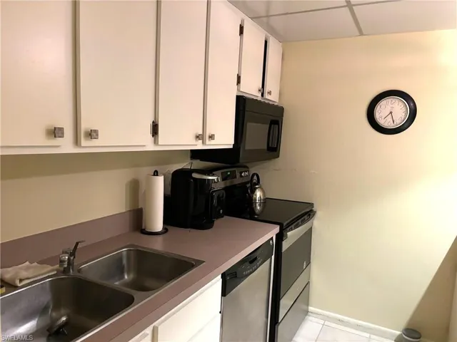 Kitchen with appliances with stainless steel finishes, a drop ceiling, sink, light tile patterned floors, and white cabinets