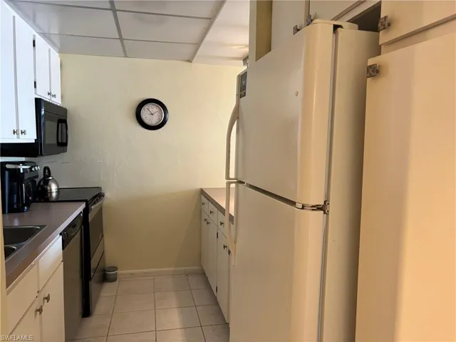 Kitchen with a paneled ceiling, sink, appliances with stainless steel finishes, light tile patterned flooring, and white cabinetry