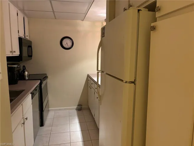 Kitchen featuring a paneled ceiling, white cabinets, light tile patterned floors, and appliances with stainless steel finishes