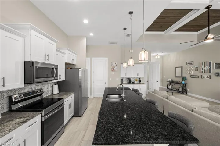 Kitchen with stainless steel appliances, open floor plan, dark stone countertops, white cabinetry, and recessed lighting