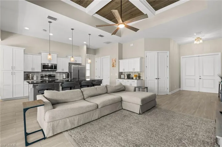 Living room featuring coffered ceiling, beamed ceiling, light wood-style floors, a ceiling fan, and a high ceiling