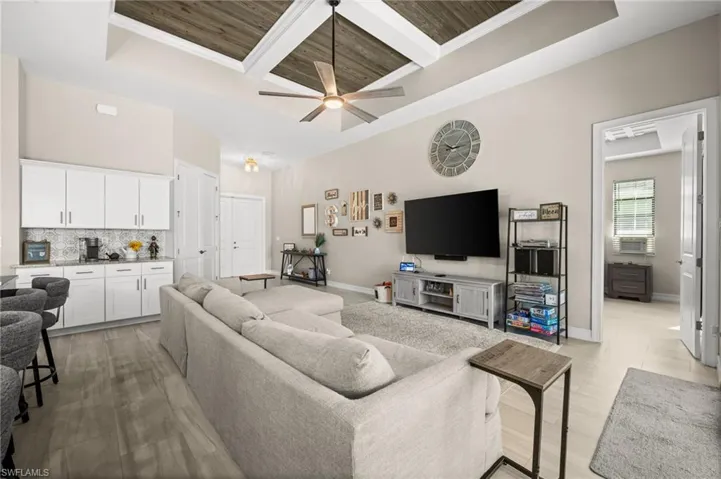 Living room with a wooden ceiling with exposed beams, coffered ceiling, ornamental molding, a ceiling fan, and a raised ceiling