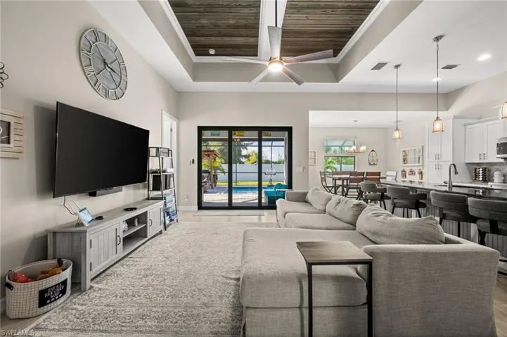 Living room featuring ceiling fan, wooden ceiling, light wood finished floors, crown molding, and a towering ceiling