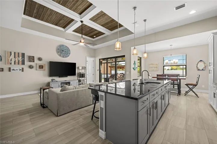 Kitchen featuring coffered ceiling, open floor plan, dark stone countertops, decorative light fixtures, and a breakfast bar