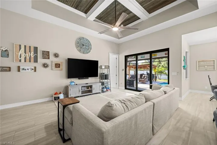 Living room featuring coffered ceiling, a towering ceiling, beamed ceiling, ceiling fan, and wood tiled floors