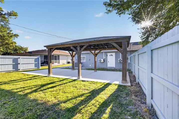 Expansive backyard featuring a large concrete patio, a substantial wooden pergola with a dark roof, and a manicured lawn
