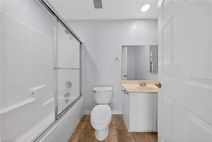 Bathroom featuring a tub/shower combination with sliding glass doors, a vanity with a light-toned countertop, a rectangular mirror, and wood-finish flooring