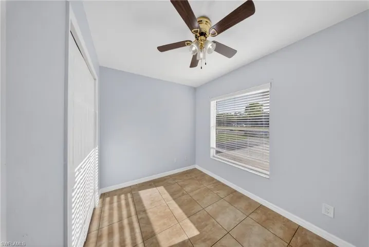 Room featuring tiled flooring, a ceiling fan with integrated lighting, a window with horizontal blinds, and a built-in closet with louvered doors