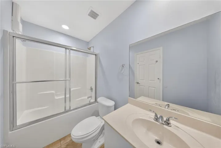 Bathroom featuring a shower-tub combination with sliding glass doors, a vanity with an integrated sink, a large wall-mounted mirror, and tile flooring