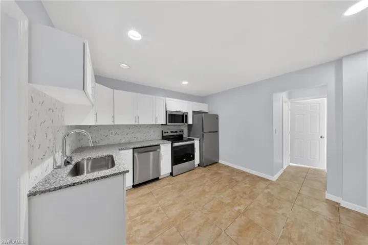 Modern kitchen featuring white cabinetry, stainless steel appliances, granite-style countertops, and a full tile backsplash