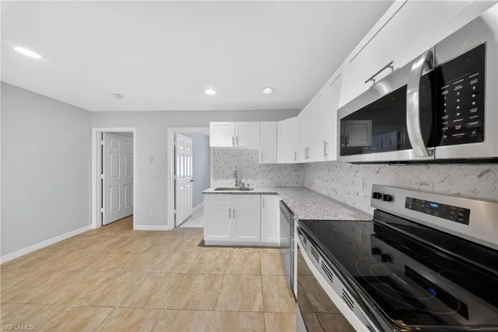 Contemporary kitchen featuring white cabinetry, stainless steel appliances, a honeycomb tile backsplash, and a light-toned countertop