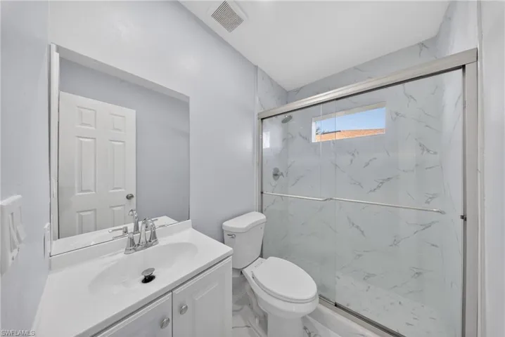 Bathroom featuring a glass-enclosed shower with full-height marble-look tile surround and a small privacy window