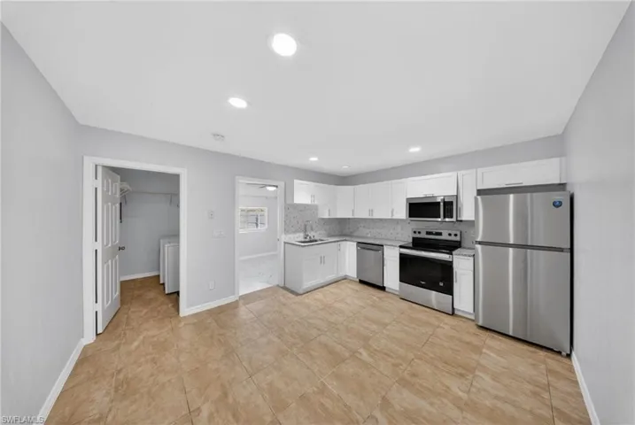 Kitchen featuring white cabinetry, stainless steel appliances, speckled countertops, and a full tile backsplash