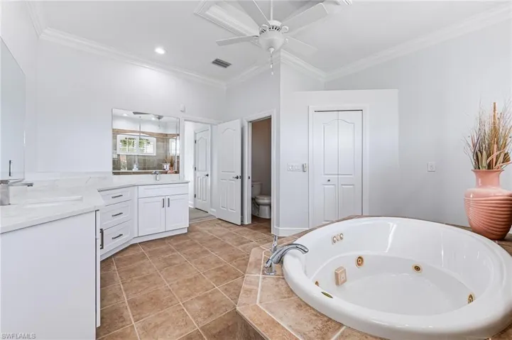 Bathroom featuring tiled tub, ornamental molding, ceiling fan, vanity, and toilet