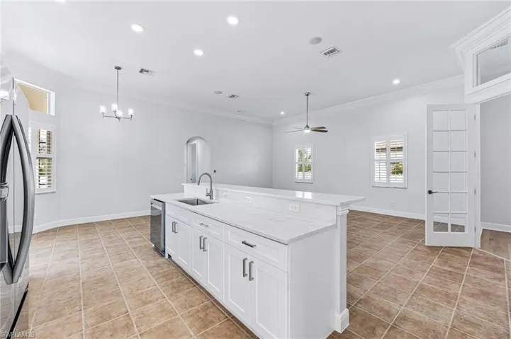 Kitchen with white cabinets, ceiling fan with notable chandelier, crown molding, a kitchen island with sink, and sink