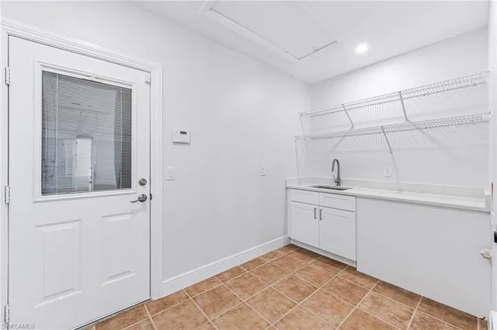 Clothes washing area with light tile patterned flooring and sink