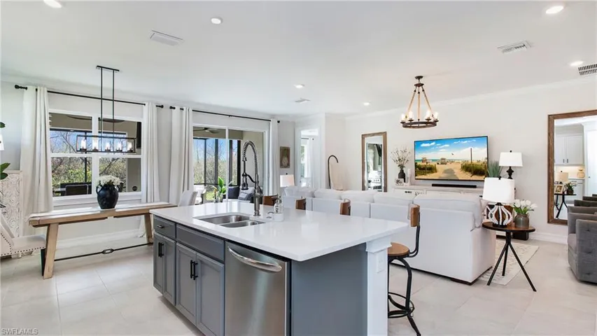 Kitchen featuring a center island with sink, sink, gray cabinetry, crown molding, and decorative light fixtures