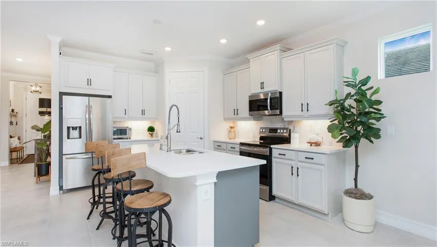 Kitchen with backsplash, stainless steel appliances, white cabinets, a breakfast bar area, and a center island with sink