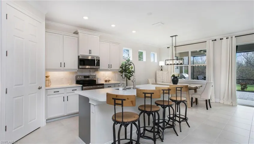Kitchen featuring white cabinetry, stainless steel appliances, decorative light fixtures, and an island with sink