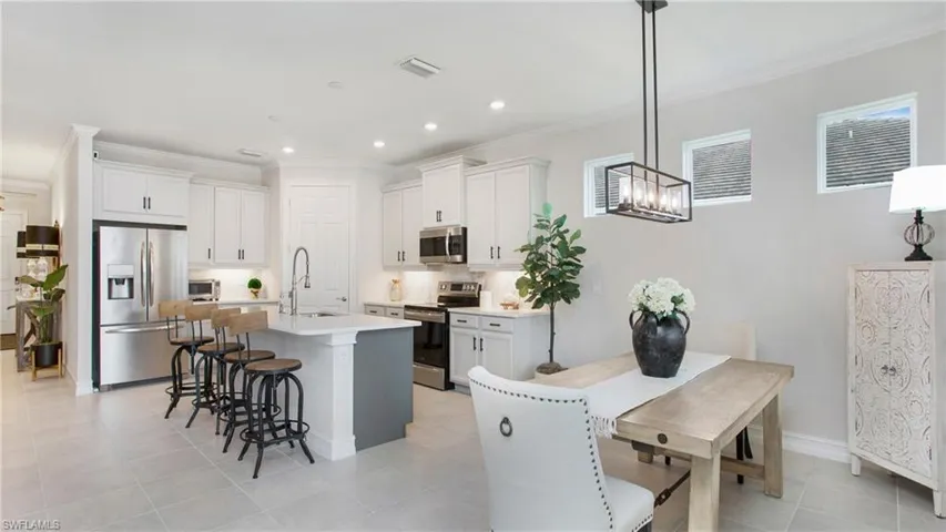 Kitchen featuring appliances with stainless steel finishes, hanging light fixtures, a kitchen island with sink, and white cabinetry